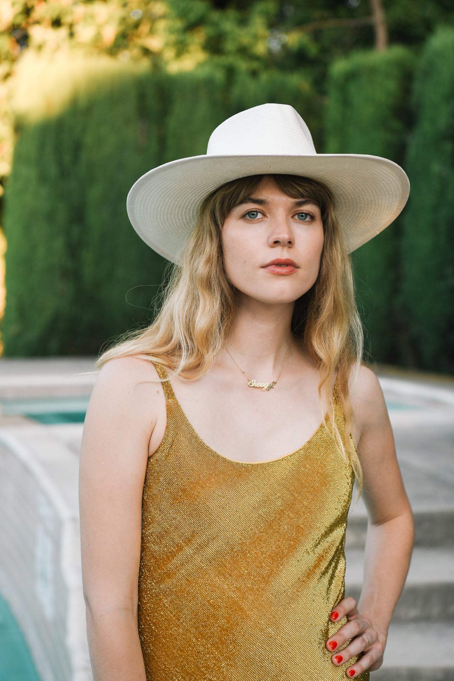 Woman in gold shimmery dress and white hat by poolside - Sunset Park Resort shop_name